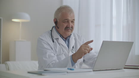 kind-cheerful-doctor-is-consulting-online-working-by-internet-with-patient-chatting-by-video-call-from-his-laptop-modern-telemedicine